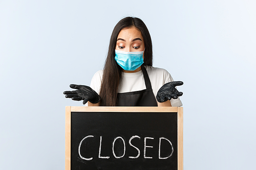 Small business, covid-19 pandemic, preventing virus and employees concept. Bothered and confused asian female entrepreneur, cafe owner complaining on coronavirus lockdown, stare at closed sign.