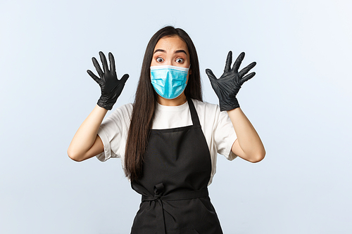 Covid-19, social distancing, small coffee shop business and preventing virus concept. Ambushed and worried young asian employee, cafe worker in medical mask and gloves raise hands up excited.
