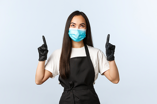 Covid-19 pandemic, social distancing, small business, preventing virus concept. Happy smiling asian coffee shop owner, barista in medical mask and gloves pointing looking at upper banner, top promo.