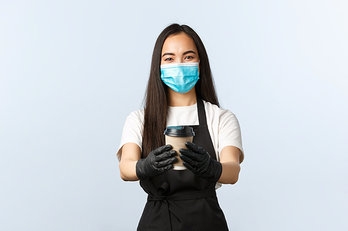 Covid-19, social distancing, small coffee shop business and preventing virus concept. Smiling cute asian female barista, waitress in medical mask and gloves, handing consumer their coffee in takeaway.