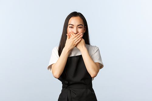 Coffee shop, small business and startup concept. Cute and silly asian female cafe employee chuckle over funny joke. Barista in black apron cover mouth as giggle with staff coworker.