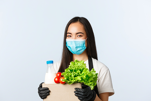 Covid-19, grocery store, employment, small business and preventing virus concept. Smiling cute asian female shop worker, cashier in medical mask and gloves taking care of your groceries order.