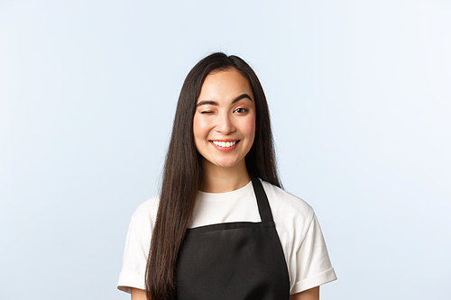 Coffee shop, small business and startup concept. Friendly and cheeky, attractive asian barista, female cafe or shop worker in black apron smiling and wink at client.