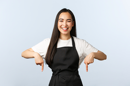 Coffee shop, small business and startup concept. Cheerful friendly asian barista in black apron showing advertisement. Pretty cafe owner inviting for special offer, pointing fingers down at banner.