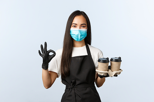 Covid-19, social distancing, small coffee shop business and preventing virus concept. Cute asian barista, cafe owner in medical mask and gloves, assure all good, guarantee as serving takeaway coffee.