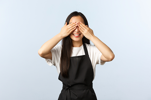 Coffee shop, small business and startup concept. Cute young asian female barista in black apron, cafe staff waiting for surprise with closed eyes, smiling anticipating, white background.