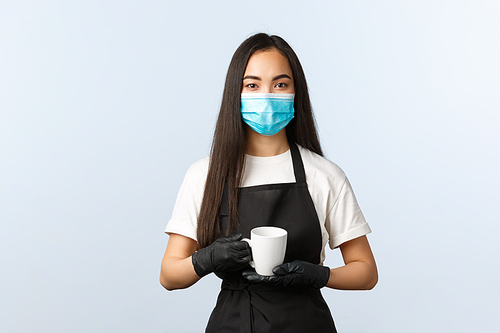 Covid-19, social distancing, small coffee shop business and preventing virus concept. Young pleasant asian female worker, barista serving coffee order in white mug, wear medical mask and gloves.