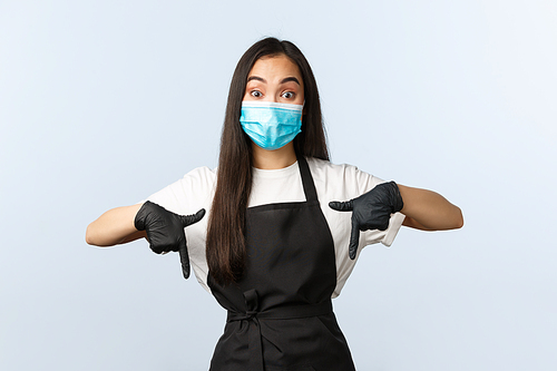 Covid-19 pandemic, social distancing, small business and preventing virus concept. Enthusiastic asian employee, barista or cafe staff in medical mask and gloves pointing down.