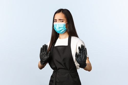 Covid-19, social distancing, coffee shop and preventing virus concept. Disgusted and reluctant asian female employee, cafe staff step away, raise hands in rejection, wear medical mask and gloves.