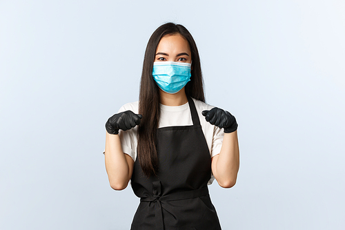 Covid-19 pandemic, social distancing, small business and preventing virus concept. Reluctant young annoyed cafe shop staff, barista or waitress in medical mask and gloves, clenching fists.