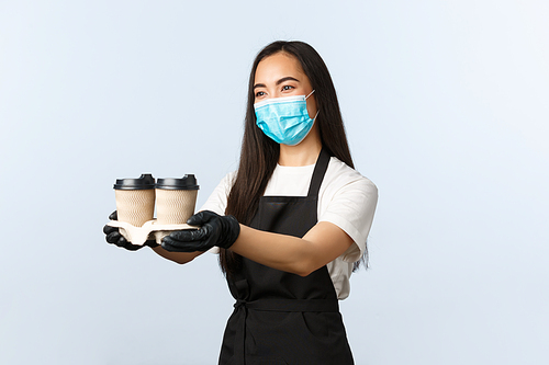 Covid-19, social distancing, small coffee shop and preventing virus concept. Nice friendly asian female barista, waitress in cafe, medical mask and gloves, handing visitor coffee in takeaway cups.
