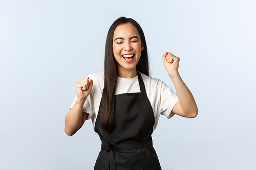 Coffee shop, small business and startup concept. Rejoicing satisfied female barista fist pump. Asian cafe staff in black apron celebrating victory, triumphing and scream yes excited.
