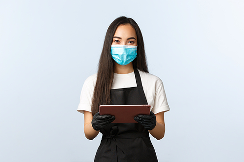 Covid-19, online orders, small coffee shop business and preventing virus concept. Friendly-looking asian female barista ready take your order, wear medical mask and gloves, hold digital tablet.