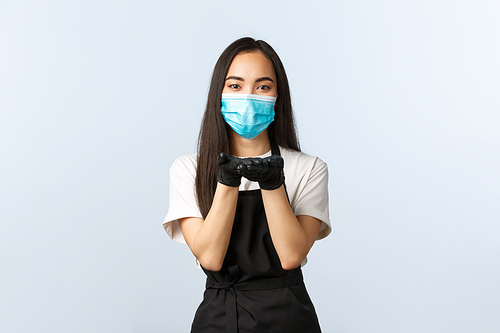Covid-19, social distancing, small coffee shop business and preventing virus concept. Cute young asian waitress, barista in medical mask and gloves hold hands near lips as if blowing kiss.