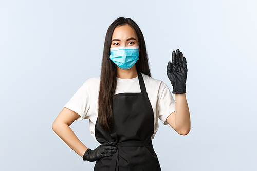Covid-19 pandemic, social distancing, small business and preventing virus concept. Friendly female barista in medical mask and gloves saying hi to clients, welcome consumer and take order at cafe.