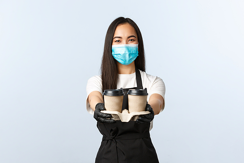 Covid-19, social distancing, small coffee shop business and preventing virus concept. Friendly pleasant asian waitress, cafe barista in medical mask serving coffee, handing order with takeaway cups.