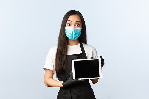 Covid-19, social distancing, small coffee shop business and preventing virus concept. Asian barista in medical mask and gloves showing client digital tablet screen, looking amazed.