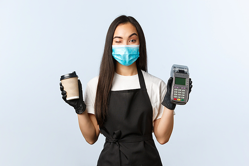 Coffee shop, coronavirus, social distancing and contactless payment concept. Cheeky cute asian waitress, barista in medical mask and gloves, wink as handing coffee order and paying terminal.