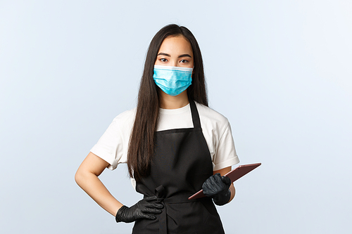 Covid-19, social distancing, small coffee shop business and preventing virus concept. Serious cute asian female barista, waitress taking client order with digital tablet, wear medical mask and gloves.