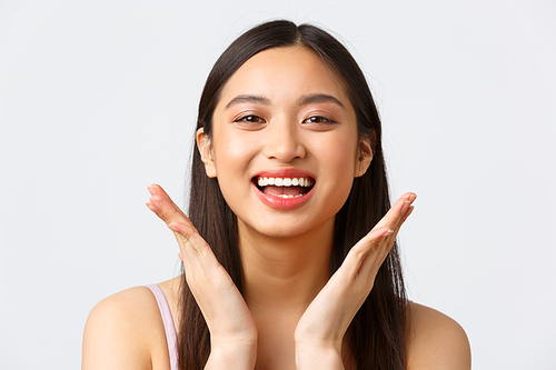 Concept of beauty, fashion and makeup products advertisement. Close-up of beautiful asian girl showing her skincare products on face, delighted with makeup, smiling upbeat.