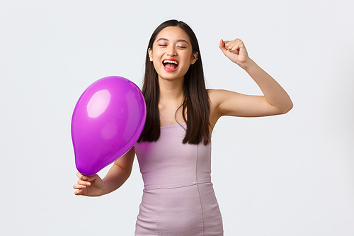 Celebration, party and holidays concept. Carefree happy asian woman in evening dress, celebrating event or birthday, dancing with colored balloon, close eyes and smiling upbeat.