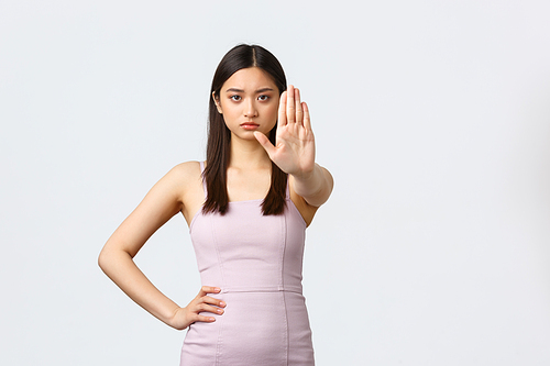 Luxury women, party and holidays concept. Serious determined asian woman in evening dress telling to stop, say enough or no, frowning and extend hand in prohibition gesture, white background.