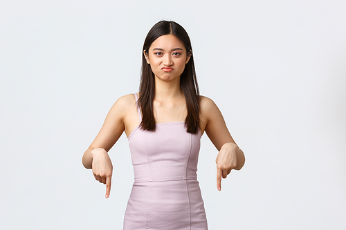 Luxury women, party and holidays concept. Picky and skeptical cute asian girl in evening dress, complaining about bad quality, pointing fingers down and grimacing displeased.