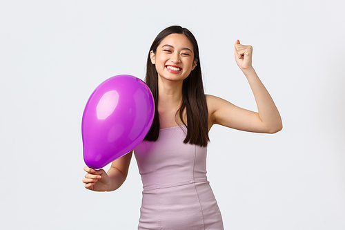 Celebration, party and holidays concept. Carefree happy asian woman in evening dress, celebrating event or birthday, dancing with colored balloon, close eyes and smiling upbeat.