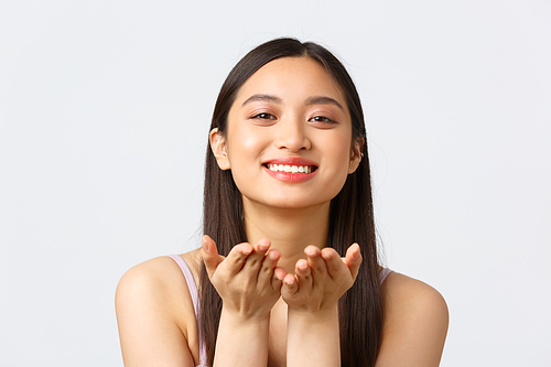 Beauty, fashion and people emotions concept. Close-up portrait of adorable romantic smiling asian girl in dress, sending air kiss and grinning happy, standing cheerful over white background.