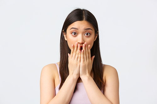 Beauty, fashion and people emotions concept. Close-up portrait of shocked, amazed and surprised asian girl, gasping cover mouth as hear revelation or gossip, standing white background.