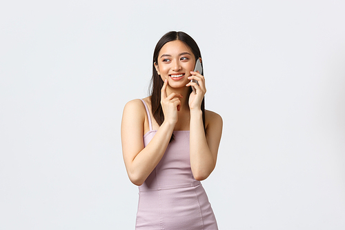 Luxury women, party and holidays concept. Romantic cute asian woman in evening dress, smiling and gazing left as talking on phone, having friendly conversation, white background.