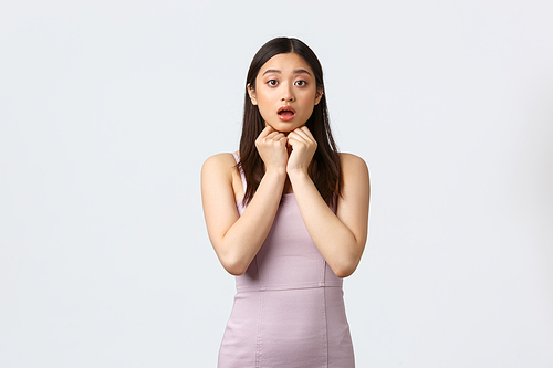 Celebration, beauty and glamour concept. Worried and concerned pretty asian woman in evening dress, looking surprised and confused, open mouth and look camera, white background.
