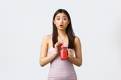 Healthy lifestyle, people emotions and leisure concept. Concerned and confused cuty silly asian woman in dress, drinking smoothie, looking troubled camera, white background.