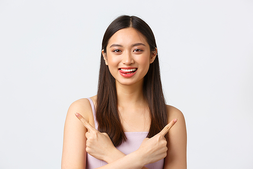 Beauty, fashion and people emotions concept. Close-up portrait of happy pretty asian girl in dress, smiling and show tongue tempting try new products, pointing fingers sideways, white background.