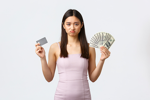 Luxury women, party and holidays concept. Moody and upset cute asian girl pouting and complaining having not enough money, showing cash and credit card with disappointed face.