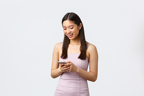Luxury women, party and holidays concept. Young attractive asian girl in evening dress texting boyfriend, smiling at mobile phone screen, messaging or using social media app.