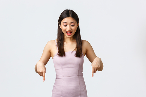 Luxury women, party and holidays concept. Enthusiastic happy pretty asian female student in prom dress, celebrating, looking and pointing fingers down with broad smile, like awesome promo offer.