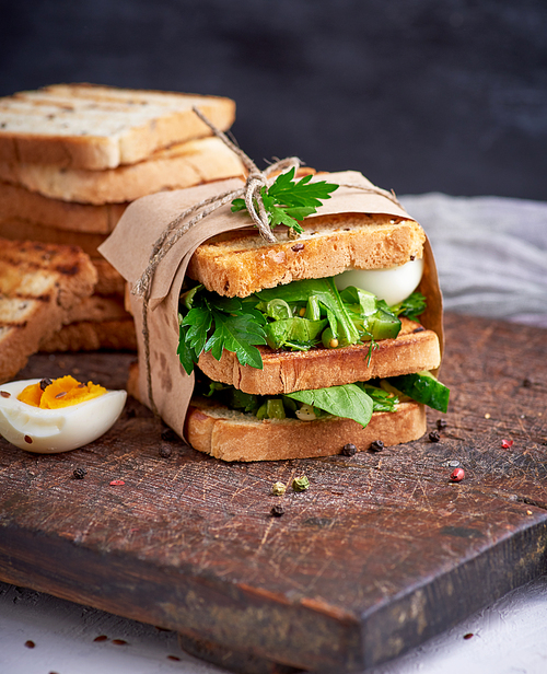 sandwich of French toast and lettuce leaves and boiled egg, a vegetarian food wrapped in paper