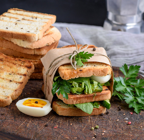 sandwich of French toast and lettuce leaves and boiled egg, a vegetarian food wrapped in paper