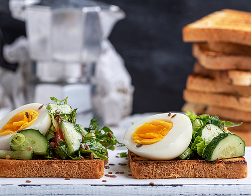 toasted square pieces of bread from white wheat flour with boiled egg, cucumber and green spinach leaves , close up