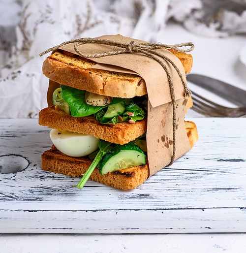 sandwich of French toast and lettuce leaves and boiled egg, a vegetarian food wrapped in paper