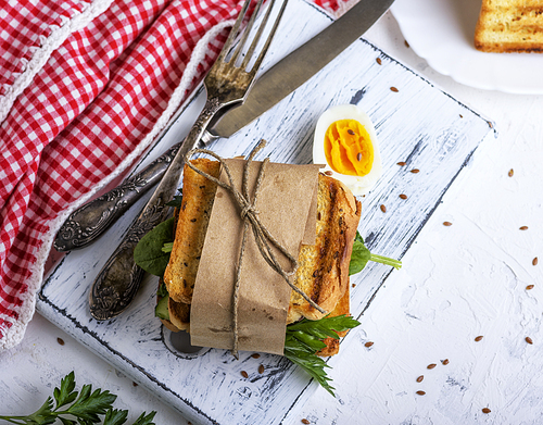 a sandwich with vegetables and an egg wrapped in paper on a white board, top view