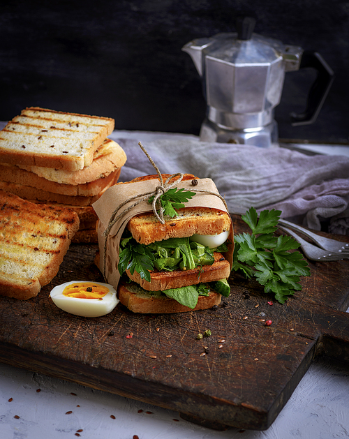 sandwich of French toast and lettuce leaves and boiled egg, a vegetarian food wrapped in paper on a wooden board