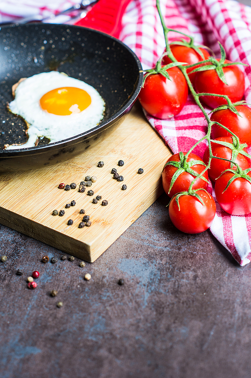Breakfast with fried egg, cherry-tomatoes and spices on rustic kitchen table