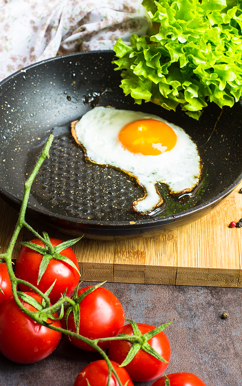 Breakfast with fried egg, cherry-tomatoes and spices on rustic kitchen table