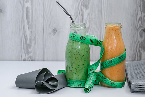 Seasonal Matcha green vegan smoothie and pumpkin carrot smoothie drink detox Breakfast with measuring tape and rubber resistance band. Stretch fitness band. Clean eating, weight loss, healthy dieting food concept. Staying healthy at home