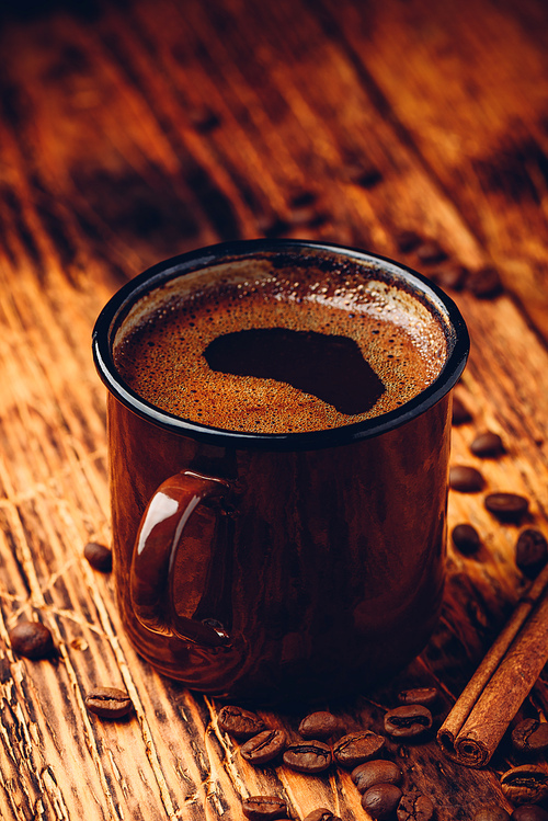 Brewed black coffee in metal mug over wooden surface