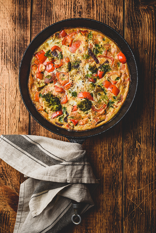 Vegetable frittata with broccoli, red bell pepper and herbs in cast iron skillet. View from above