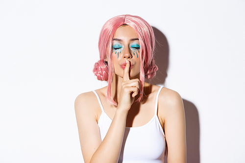 Close-up of lovely girl with pink wig and bright makeup, close eyes and shushing, have surprise or secret, standing over white background.