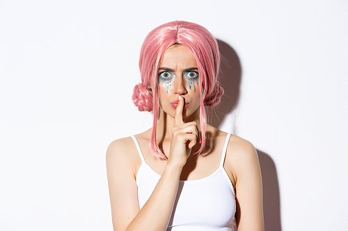 Close-up of angry girl with pink wig, frowning and shushing with mad face, standing over white background.